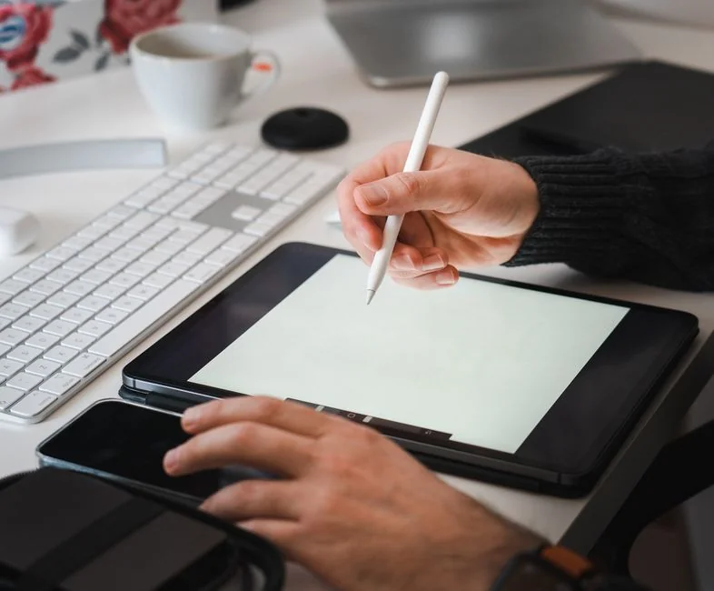 Business professional using a tablet and laptop with a hot drink, focusing on digital content review.